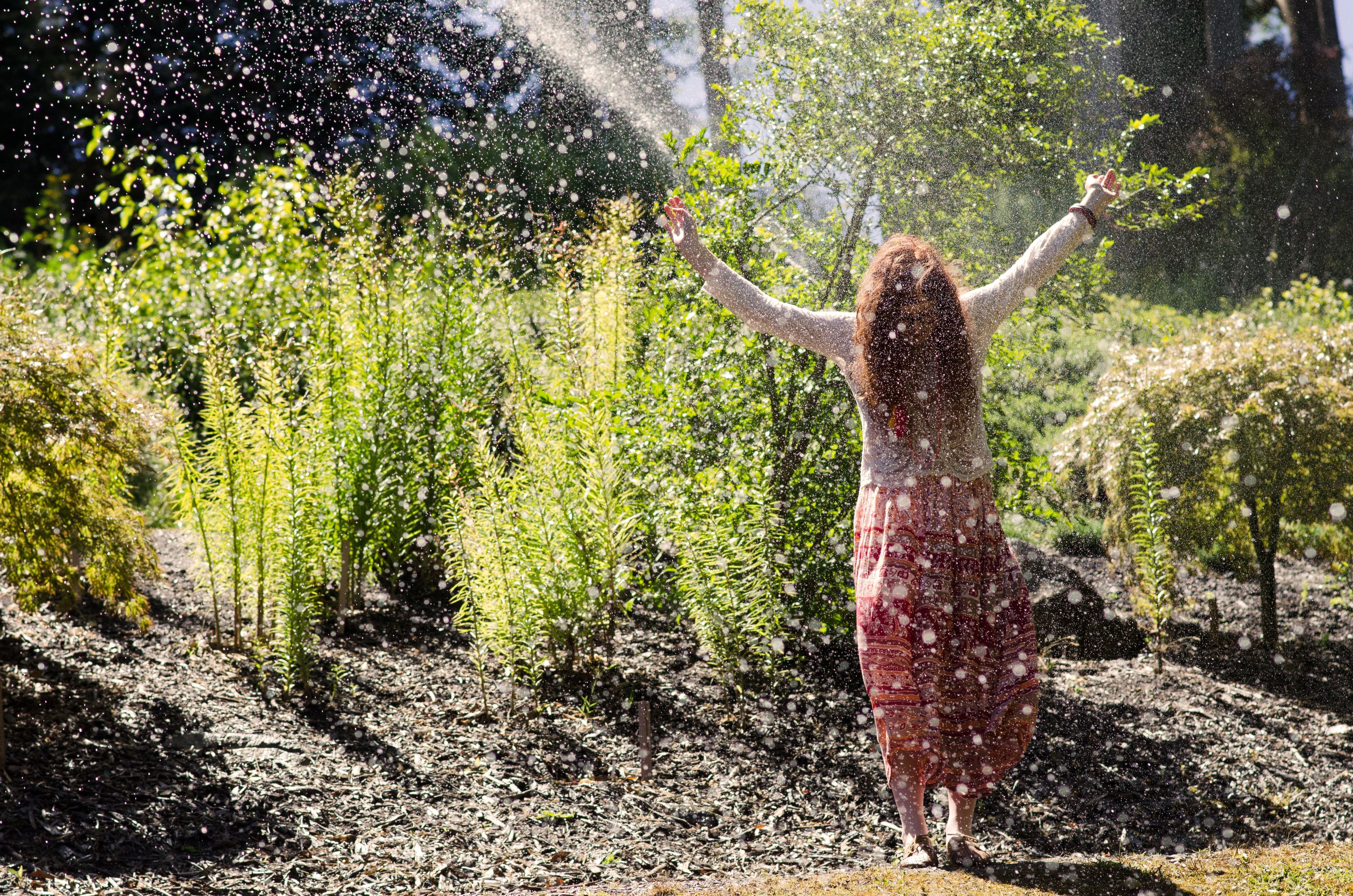 a woman in front of plants playing in a water spraying in the air