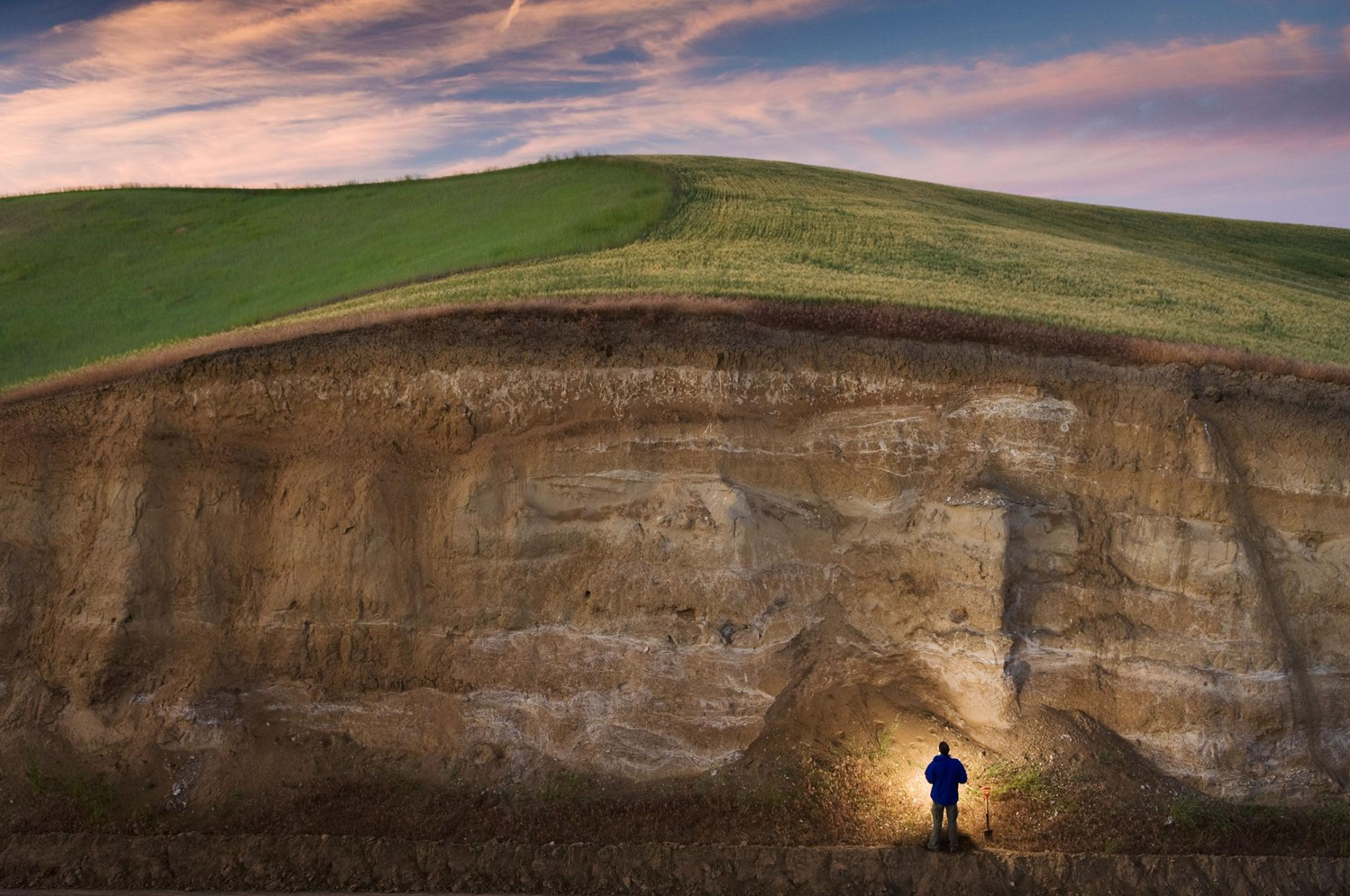 a man holding a flashlight looking at a large wall of soil